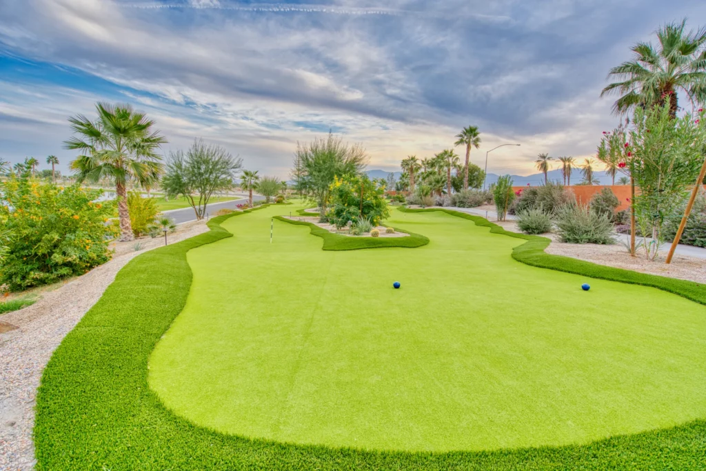 A landscaped mini-golf course with putting greens, surrounding plants, palm trees, and a partly cloudy sky.