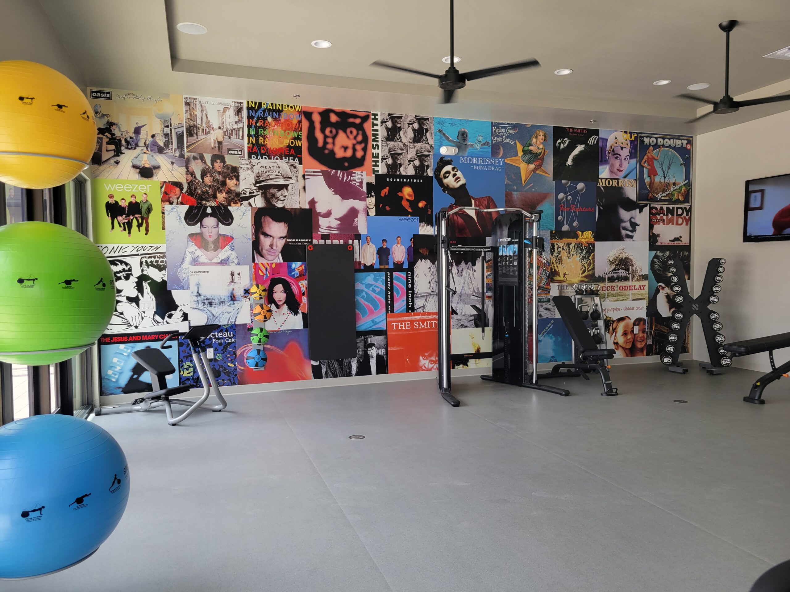 A gym with colorful exercise balls and equipment, featuring a wall covered in music album covers and posters.