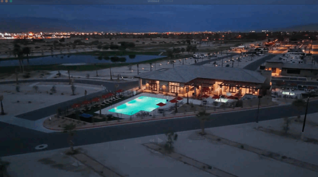 Aerial view of a modern building with an illuminated outdoor swimming pool at dusk, surrounded by desert landscape and distant city lights.
