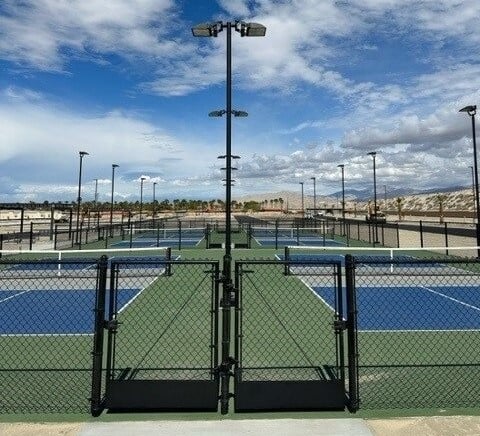 A fenced outdoor pickleball court complex with multiple blue and green courts under a partly cloudy sky.
