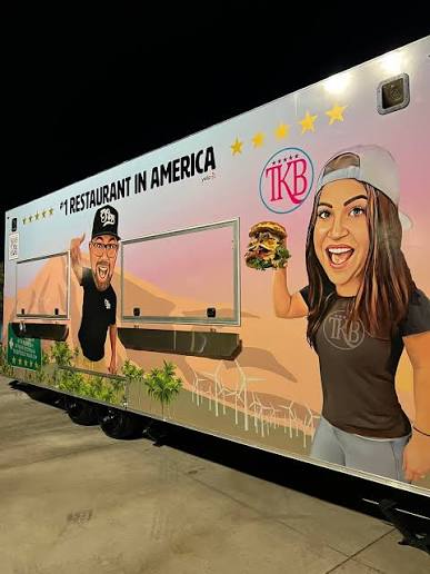 A food truck features cartoon images of a smiling man and woman; she holds a burger and wears a TKB shirt. Text above reads "No. 1 Restaurant in America.